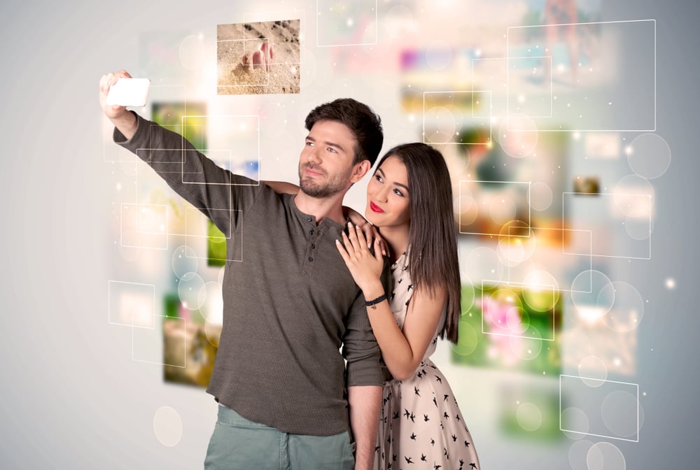 Collecting memories concept with photos in backbround and a happy young couple in love taking selfie with a mobile phone